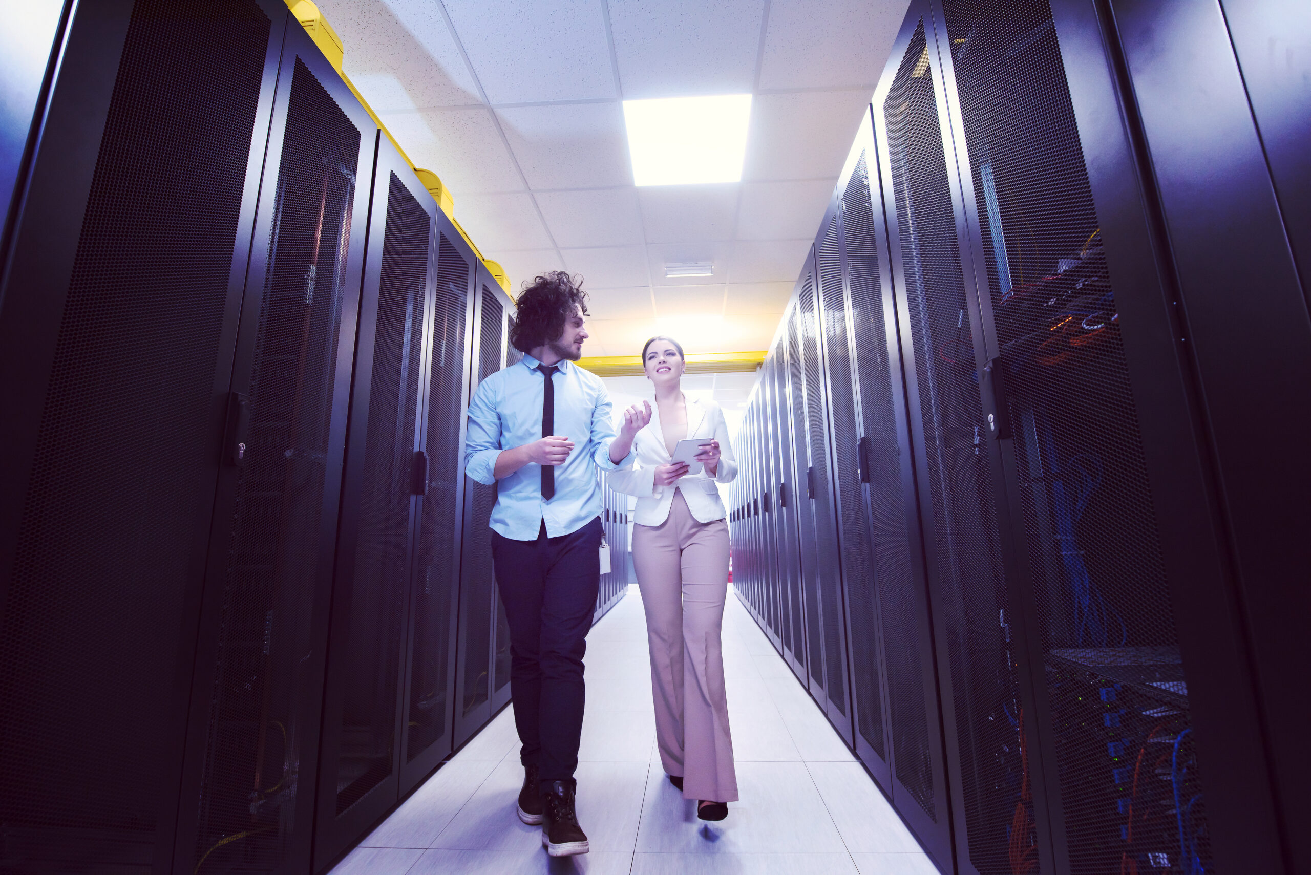 Young IT engineer showing working data center server room to female chief engineer who holding tablet computer